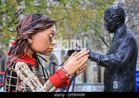 Westminster, London, Großbritannien. 7th Dez 2021. Little Amal mit der Statue von Nelson Mandela auf dem Parliament Square. Die kleine Amal, die riesige Marionette, die ein kleines Flüchtlingsmädchen darstellt, ist heute wieder im Zentrum von London und außerhalb des Parlaments, um einen Protest gegen das Gesetz über Nationalität und Grenzen zu unterstützen, das potenziell Flüchtlinge und andere, die im britischen Asylsystem Asyl suchen, behindern könnte. Die Marionette war in diesem Sommer und Herbst auf einer langen Reise von Syrien nach Großbritannien mit vielen Auftritten unterwegs gewesen. Kredit: Imageplotter/Alamy Live Nachrichten Stockfoto