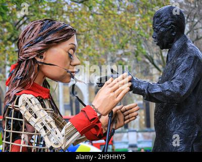 Westminster, London, Großbritannien. 7th Dez 2021. Little Amal mit der Statue von Nelson Mandela auf dem Parliament Square. Die kleine Amal, die riesige Marionette, die ein kleines Flüchtlingsmädchen darstellt, ist heute wieder im Zentrum von London und außerhalb des Parlaments, um einen Protest gegen das Gesetz über Nationalität und Grenzen zu unterstützen, das potenziell Flüchtlinge und andere, die im britischen Asylsystem Asyl suchen, behindern könnte. Die Marionette war in diesem Sommer und Herbst auf einer langen Reise von Syrien nach Großbritannien mit vielen Auftritten unterwegs gewesen. Kredit: Imageplotter/Alamy Live Nachrichten Stockfoto