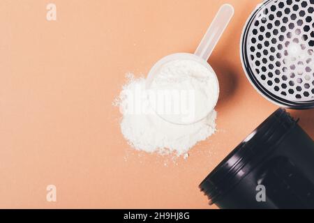 Schaufel und Shaker-Becher aus Proteinpulver für die Herstellung von Sportcocktails auf braunem Hintergrund, flach liegend Stockfoto