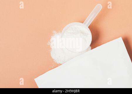 Proteinpulver aus Öko-Papiertüte im Messlöffel streut auf braunem Hintergrund mit Kopierfläche, flach liegend Stockfoto