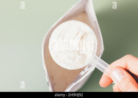 Proteinpulver Messlöffel in weiblicher Hand über offener Packung des Produktes auf grünem Hintergrund, Draufsicht Stockfoto