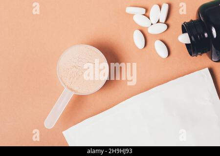 Molkenproteinpulver im Messlöffel neben Aminosäurepillen, Sporternährungsergänzungen auf braunem Hintergrund, flach liegend Stockfoto