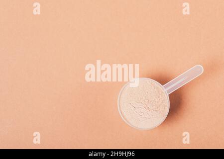 Schokoladenproteinpulver im Messlöffel auf braunem Hintergrund mit Kopierraum, flach liegend Stockfoto