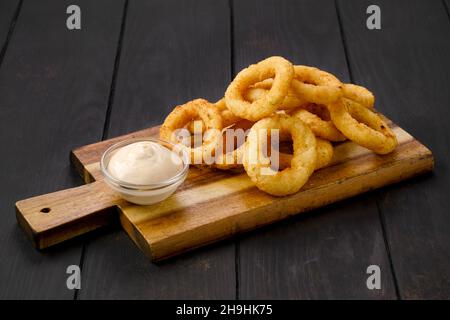 Frittierte panierte Tintenfischringe mit cremiger Sauce auf einem hölzernen Servierbrett Stockfoto