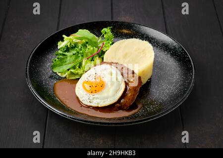 Rinderschnitzel mit Spiegelei, Kartoffelpüree und frischem Salat auf einem Teller Stockfoto