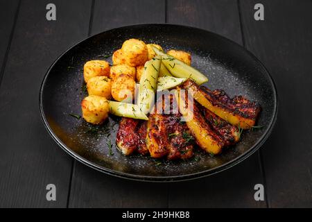 Gebratener Schweinebauch mit Kartoffelbällchen und eingelegter Gurke auf einem Teller Stockfoto