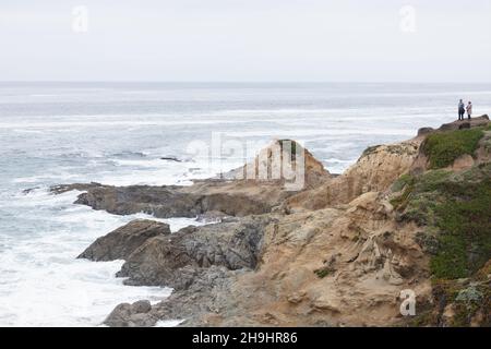Ein Paar, das aus der Ferne auf einer felsigen Klippe in Bodega Head an der Küste von Sonoma County, Kalifornien, steht. Stockfoto