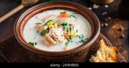 Warme finnische cremige Suppe mit Lachs und Gemüse in alter Keramikschale auf altem Holzhintergrund. Rustikaler Stil. Stockfoto