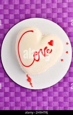 Valentinstag Hintergrund für Bäckerei, Süßwaren. Weißer Mousse-Kuchen in Herzform mit der Aufschrift Love auf violettem Hintergrund Stockfoto