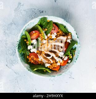 Salat mit roten Linsen, Spinatblättern, Kirschtomaten, Hühnerfleisch und Mozzarella-Käse mit Olivenöl in Keramikplatte auf altem betongrauen Backg Stockfoto