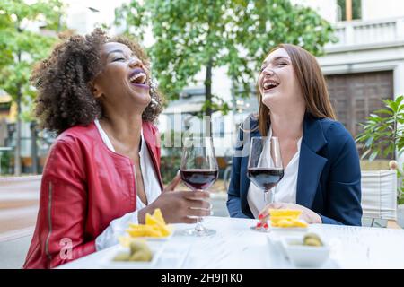 Zwei glückliche Freundinnen, die mit Rotwein lachen und toasten, Erwachsene, die eine Pause von der Arbeit genießen, Mittagspausen nach einem harten Arbeitstag, woome Stockfoto