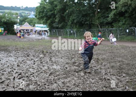 Ein kleines Kind, das am ersten Tag des Glastonbury 2016 durch Schlamm spazierend ist. Aus einer Serie von Fotos, die Menschen zeigen, die am ersten Tag in Glastonbury 2016 auf der Worthy Farm im Regen eintreffen Stockfoto