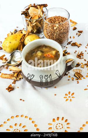 Glutenfreie Buchweizensuppe mit Gemüse, Kartoffeln und Pilzen in einer Schüssel auf weißem Tischtuch, bestreut mit getrocknetem Samen, Pilzen und Kartoffeln. Stockfoto