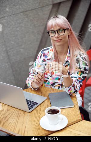 Smarte Frau in Gläsern, die am Kaffeetisch im Freien sitzt Stockfoto
