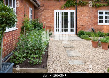 Cottage Garden Großbritannien. Kleiner Garten mit harter Landschaft, Kies und York Steinpflaster, hölzernen Fenstertüren und Gemüsebetten Stockfoto