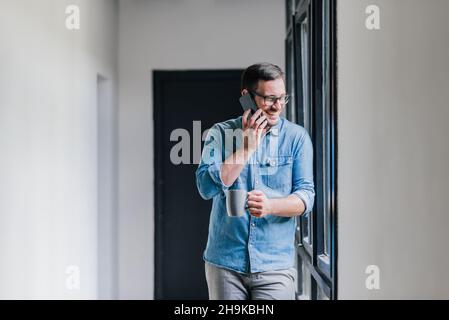 Selbstbewusst lächelnd junge erfolgreiche fröhlich casual Unternehmer Geschäftsmann auf Kaffeepause Gespräch am Telefon Anruf zufrieden Kaffee trinken Stockfoto