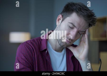 Müder Freiberufler, der im Heimbüro sitzt und Remote online arbeitet und unter Kopfschmerzen leidet Stockfoto