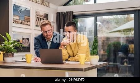 Junge erfolgreiche gemischte Rassen Paar sitzt im Wohnzimmer oder in der Küche diskutieren neue Home-Projekt mit Laptop arbeiten und planen Berechnung Heimfi Stockfoto