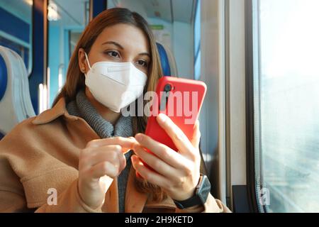 Sicherheit im öffentlichen Verkehr. Junge Frau mit FFP2 KN95 Gesichtsmaske mit Mobiltelefon im Zug. Stockfoto