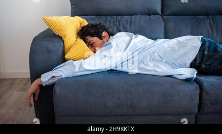 Verzweifelter Mann, der auf dem Sofa liegt und über seine Probleme nachdenkt. Porträt von müde allein ernsten Mann mit Problem in der Beziehung. Unangenehme Schmerzen bei Stockfoto