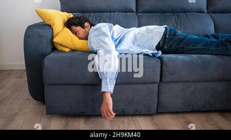 Verzweifelter Mann, der auf dem Sofa liegt und über seine Probleme nachdenkt. Porträt von müde allein ernsten Mann mit Problem in der Beziehung. Unangenehme Schmerzen bei Stockfoto