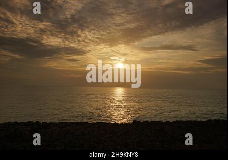Die Sonne geht über dem Meer auf, die Wolken werden von gelbem Licht beleuchtet Stockfoto