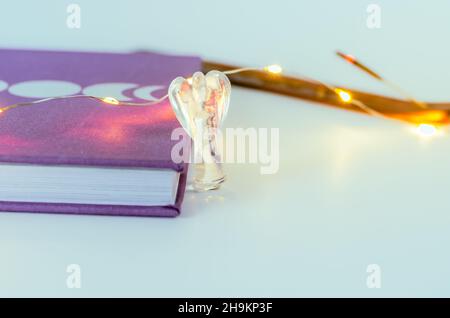 Nahaufnahme von Engelskristall aus klarem Quarz in der Nähe eines Mondjournals mit Weihnachtslichtern und Weihrauch auf dem Hintergrund. Konzept: Spirituelle Selbstversorger-Praktiken Stockfoto