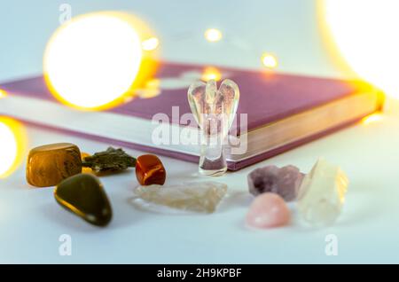 Nahaufnahme von Engelskristall aus klarem Quarz in der Nähe eines Mondjournals mit Weihnachtslichtern und Weihrauch auf dem Hintergrund. Konzept: Spirituelle Selbstversorger-Praktiken Stockfoto
