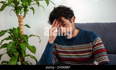 Gutaussehende männliche Modell fühlt sich müde nach der Arbeit. Reifer Mann, der seine Stirn hält, während er Kopfschmerzen hat, während er auf der Couch zu Hause sitzt. Unangenehme Schmerzen. Stockfoto