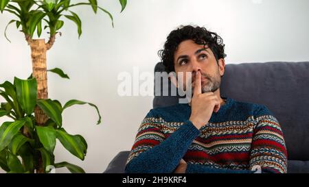Gutaussehende männliche Modell fühlt sich besorgt verwirrt in Gedanken verloren erwägen Entscheidungsfindung Konzept. Mann trägt einen Winterpullover und denkt beim Sittin nach Stockfoto