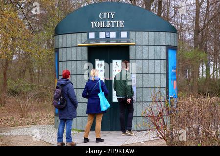 Leute schwirren an einer automatischen Selbstreinigungs-„City Toilette“ in Berlin. Die öffentlichen Toiletten sind kostenpflichtige Toiletten, für die eine Gebühr erhoben wird. Stockfoto