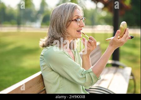 Frau, die im Spiegel schaut und Lippenstift auf die Lippen auflegt Stockfoto