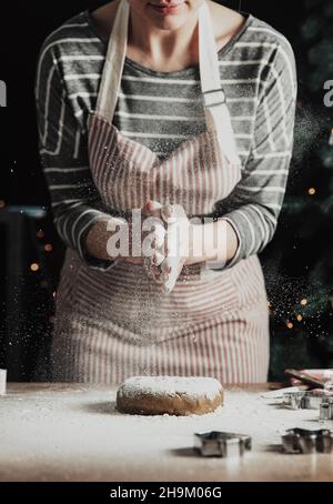 Frohe Weihnachten, Frohes neues Jahr. Lebkuchenkochen, Kuchen, Strudelbacken. Die Frau im Vorfeld bereitet Kekse vor. Handflächen schlagen, Mehl über den kneteten Teig spritzen. Junges Mädchen vorbereiten, backen, kochen Stockfoto