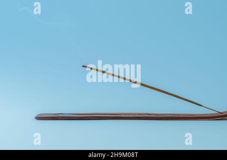 Minimalistische Nahaufnahme von brennendem Räucherstäbchen mit Rauch auf blauem Hintergrund Stockfoto