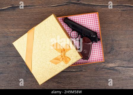 Draufsicht auf eine Makarov Pistole in einer Geschenkbox. Geschenkbox mit einer Waffe auf einem Holzhintergrund. Stockfoto