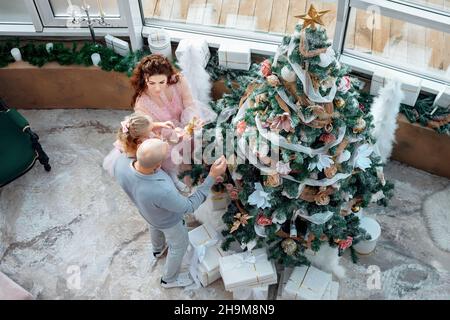 Draufsicht auf die wunderschöne kaukasische Familie, die einen Weihnachtsbaum für den Urlaub schmückt. High-Angle-Ansicht der Eltern mit Tochter Dekoration Haus. Glückliche Familie bereitet sich auf Weihnachten oder Neujahr vor. Stockfoto