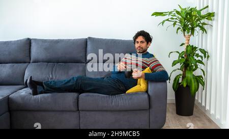 Hübscher Mann mit Bart trinkt morgens Espresso-Kaffee mit glücklichem Gesicht lächelnd und schaut auf die Kamera auf dem Sofa von zu Hause. Positive Person. Stockfoto