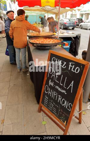 SAINT JEAN DE LUZ, FRANKREICH - 24. Mai 2019: Mann mit baskischer Mütze im Gespräch mit einem Mann, der Paella unter freiem Himmel vorbereitet Stockfoto