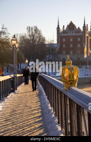 Stockholm im Winter. Menschen, die auf der Brücke mit einer vergoldeten Krone auf Skeppsholmsbron mit Strandvagen im Hintergrund laufen. Stockfoto