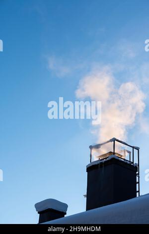 Rauch aus dem Kamin des Hauses, Heizung am kalten Wintertag, klarer blauer Himmel. Stockfoto