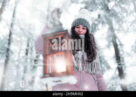 Das Mädchen hält eine Laterne mit einem Licht in der Hand und leuchtet auf ihrem Weg in den gefrorenen Wald, Weihnachten und gefrorene Atmosphäre, Bethlehem Licht leuchtet ich Stockfoto