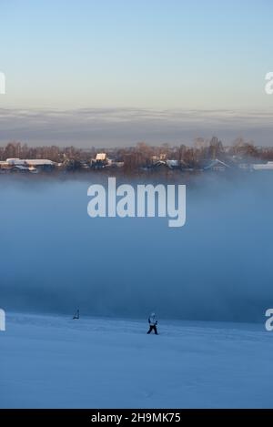 Nördliche frostige Landschaft. Nebel steigt von der Oberfläche eines ungefrorenen Flusses auf. Eine Person beschäftigt sich mit nordic Walking und spaziert durch den Schnee am vorbei Stockfoto