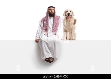 Saudi-arabischer Mann, der auf einer leeren Tafel sitzt, mit einem Retriever-Hund, der auf weißem Hintergrund isoliert ist Stockfoto