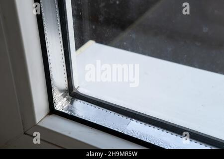 Kondensation auf dem Glas im PVC-Fenster. Problematische, fehlerhafte Verglasung der Kunststoffstruktur, an einem Wintertag. Nahaufnahme. Stockfoto