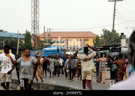 Lagos, Nigeria, 7th. Dezember 2021. Passanten heben ihre Hände, während sie an Polizeifahrzeugen am Gymnasium in Ojodu, Lagos, Nigeria, vorbeigehen, wo ein Lieferwagen, der angeblich von Verkehrsbeamten gejagt wurde, einige Schüler tötete, die von der Schule zurückkehrten. Während der Augenzeuge sagte, dass mindestens 17 Schüler starben, bestätigte die Polizei am Dienstag, dass drei Tote, 12 Verletzte, bei dem Unfall starben. Foto von Adekunle Ajayi Stockfoto