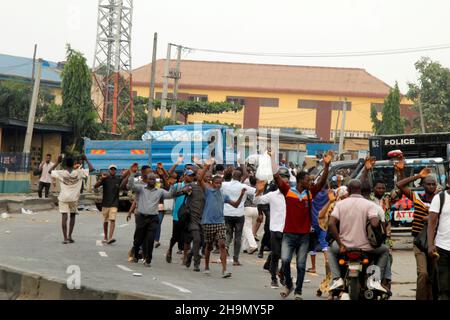 Lagos, Nigeria, 7th. Dezember 2021. Passanten heben ihre Hände, während sie an Polizeifahrzeugen am Gymnasium in Ojodu, Lagos, Nigeria, vorbeigehen, wo ein Lieferwagen, der angeblich von Verkehrsbeamten gejagt wurde, einige Schüler tötete, die von der Schule zurückkehrten. Während der Augenzeuge sagte, dass mindestens 17 Schüler starben, bestätigte die Polizei am Dienstag, dass drei Tote, 12 Verletzte, bei dem Unfall starben. Foto von Adekunle Ajayi Stockfoto