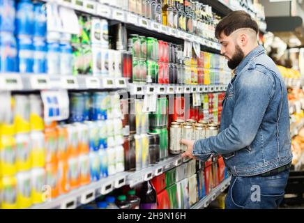 Interessierter junger Mann, der im Lebensmittelgeschäft Einkäufe tätigt und Bier aus der Dose kauft Stockfoto