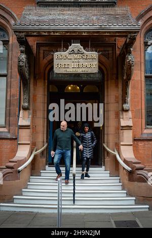 Ein Mann und eine Frau an der Vorderseite verlassen das Canterbury Royal Museum and Library in Canterbury, Kent, England. Stockfoto