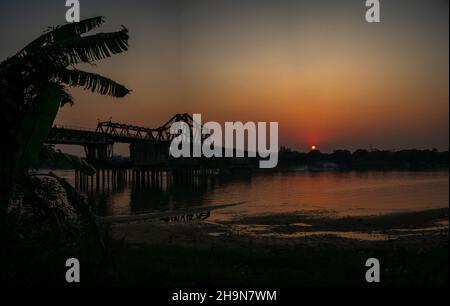 Sonnenuntergang über der Long Bien Brücke die Long Bien Brücke wurde 1902 von den Franzosen über den Roten Fluss in Hanoi, Vietnam, gebaut. Dies ist eine der ältesten Brücken Stockfoto