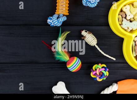 Verschiedene Accessoires für Hunde und Katzen: Mausspielzeug, Ball, Kamm, Leine, Kragen, Spielzeug und Schüssel mit Knochen auf schwarzem Holzhintergrund. Haustiere Pflege und Rout Stockfoto